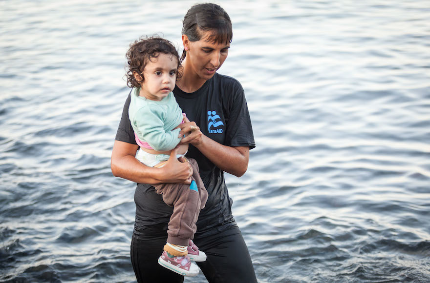 Israel Doctor Tali Shaltiel wades into the water to take a small Syrian child from a dinghy that arrived at a beach in the Greek island of Lesbos. (Boaz Arad/IsraAid)