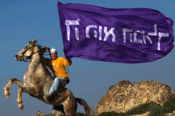 A settler rides his horse in Havat Gilad while holding a flag that says "God is the King." (Nati Shohat / Flash 90/JTA)