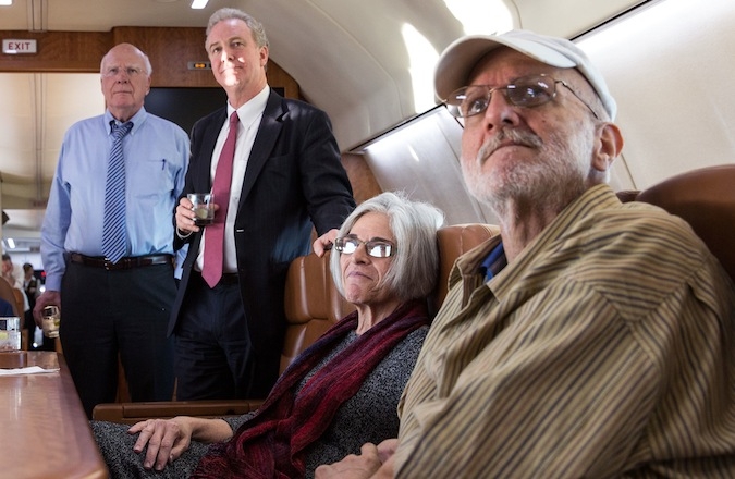 Alan Gross with his wife Judy watch television onboard a government plane headed back to the US as the news breaks of his release, while U.S. Rep. Chris Van Hollen, second from left, looks on, Dec. 17, 2014. (Wikimedia Commons)