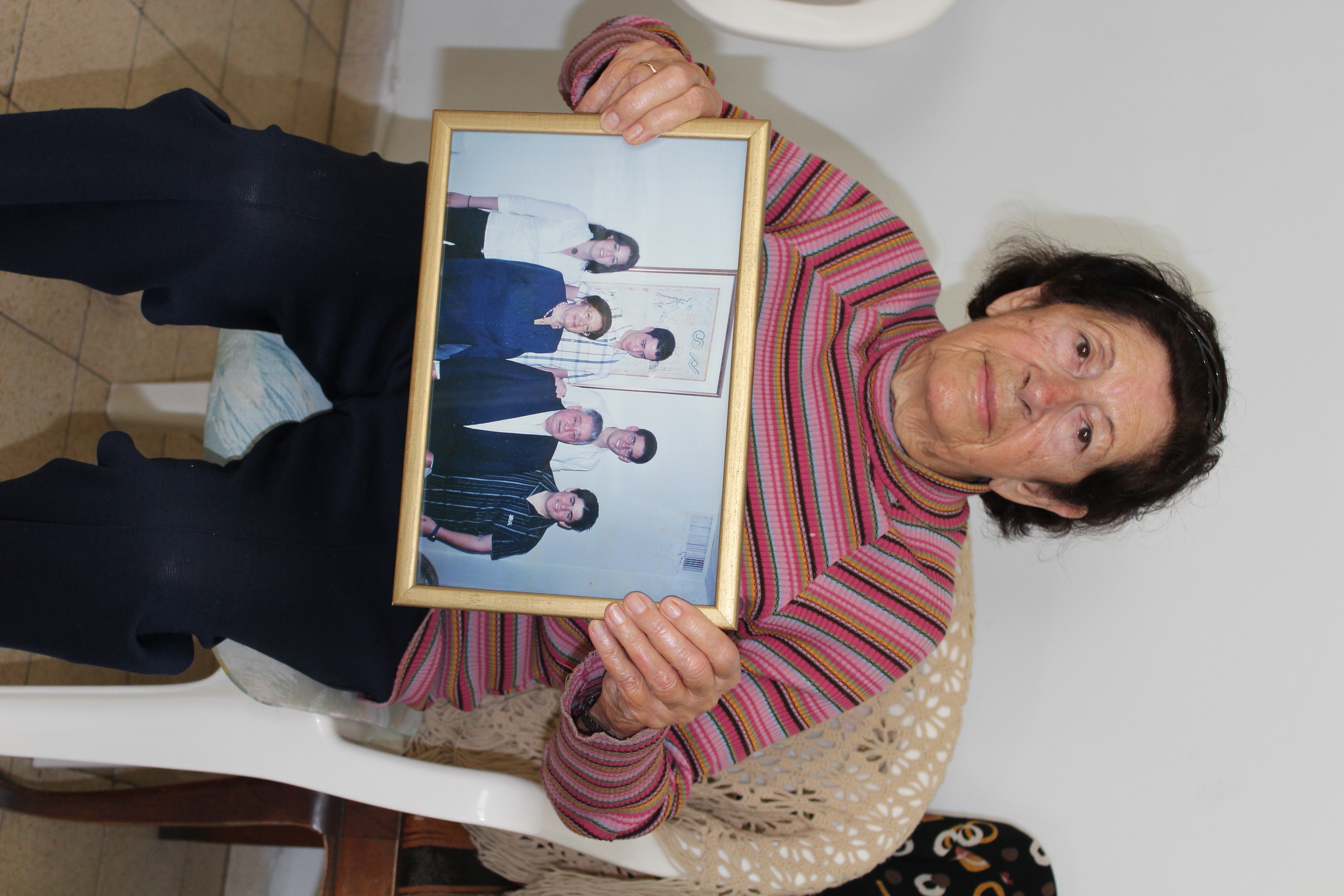Tel Aviv resident Sylvia Selvas, displaying a photo of her late husband and their four grandchildren, hoped to locate her long-lost friend from their native Greece. (Hillel Kuttler)