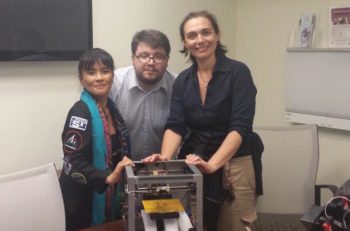 Gifford, right, looks over a 3D printer with scientists Dr. Susan Jewell and Matteo Borri. (Courtesy of Sheyna Gifford)