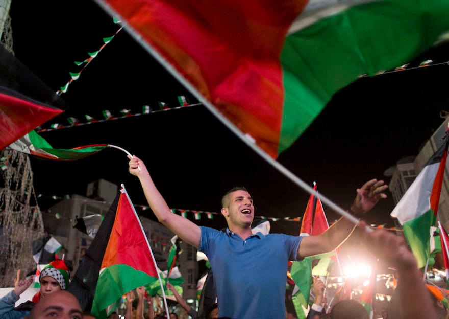 Palestinians sing and wave their national flags after a speech by Palestinian President Mahmoud Abbas at the U.N. General Assembly shown on TV in the West Bank city of Ramallah, Wednesday, Sept. 30, 2015. (AP Photo/Nasser Nasser)