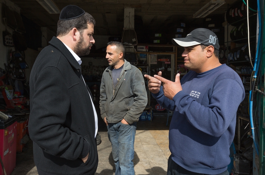 A haredi Orthodox Jewish man from the Israeli settlement of Beitar Illit talking with Arabs as he gets his car washed at the Palestinian-owned Hussan Junction car wash, in the West Bank, Nov. 11, 2015. Photo (Nati Shohat/Flash90)