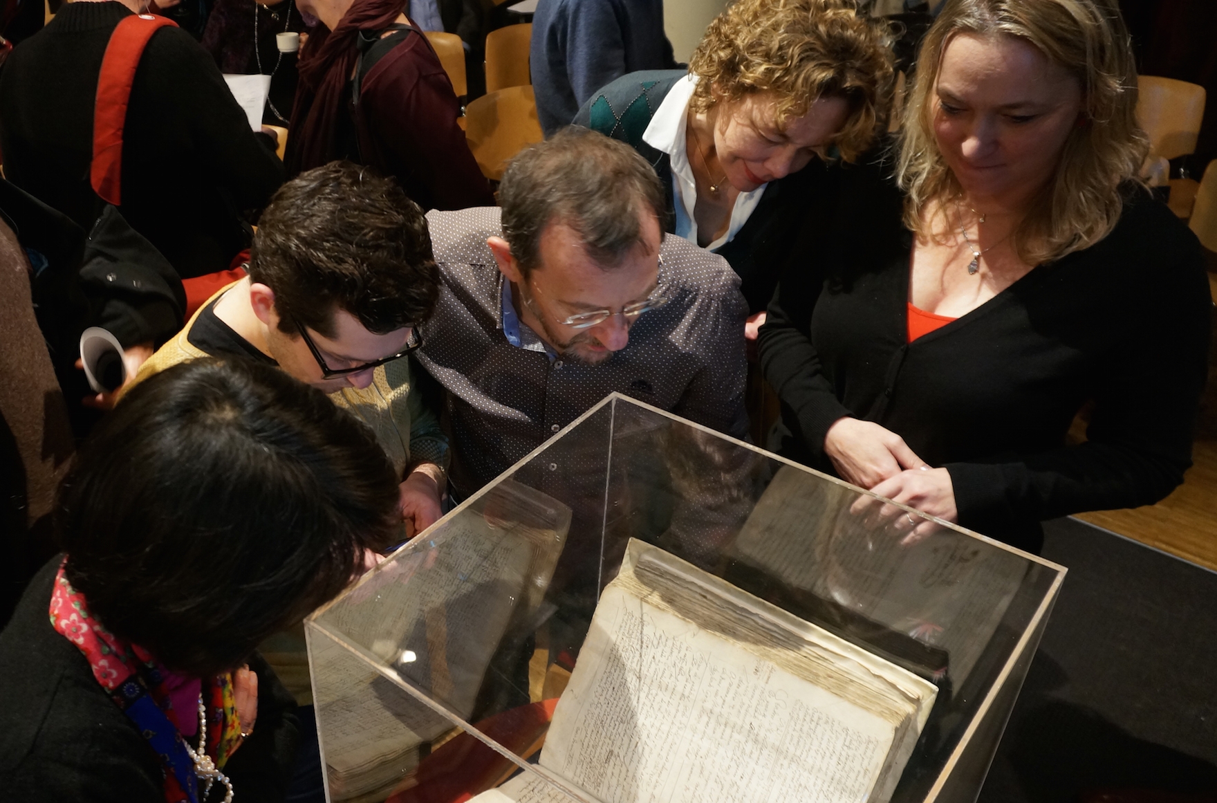 Attendees at an Amsterdam symposium on whether to lift the ancient order of excommunication against the philosopher Baruch Spinoza examining a copy of the original writ against him, Dec. 6, 2015. (Cnaan Liphshiz)