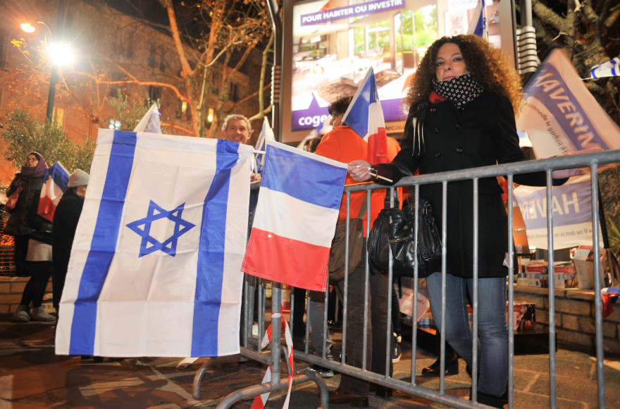 Members of France's Jewish community wave Israeli and French flag, and light memorial candles at a ceremony outside the Hyper Cacher supermarket in Paris, a year after four Jewish shoppers were killed in a terror attack on the store. (Flash90 photo/Serge Attal)