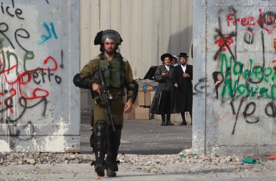 Ultra-Orthodox Jewish men standing behind a section of Israel's security fence as an Israeli soldier makes his way at the main entrance of the West Bank city of Bethlehem during clashes with Palestinian protesters, Oct. 12, 2015. (Musa al-Shaer/AFP/Getty Images)