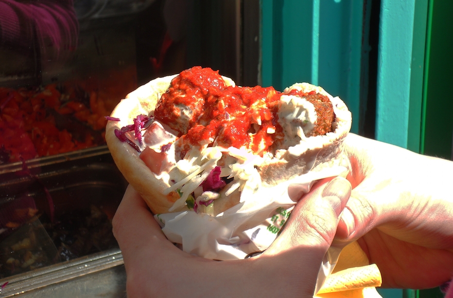 A patron of L'As du Fallafel holding the restaurant's acclaimed falafel sandwich, which is covered in hot sauce. (WikiMedia Commons)