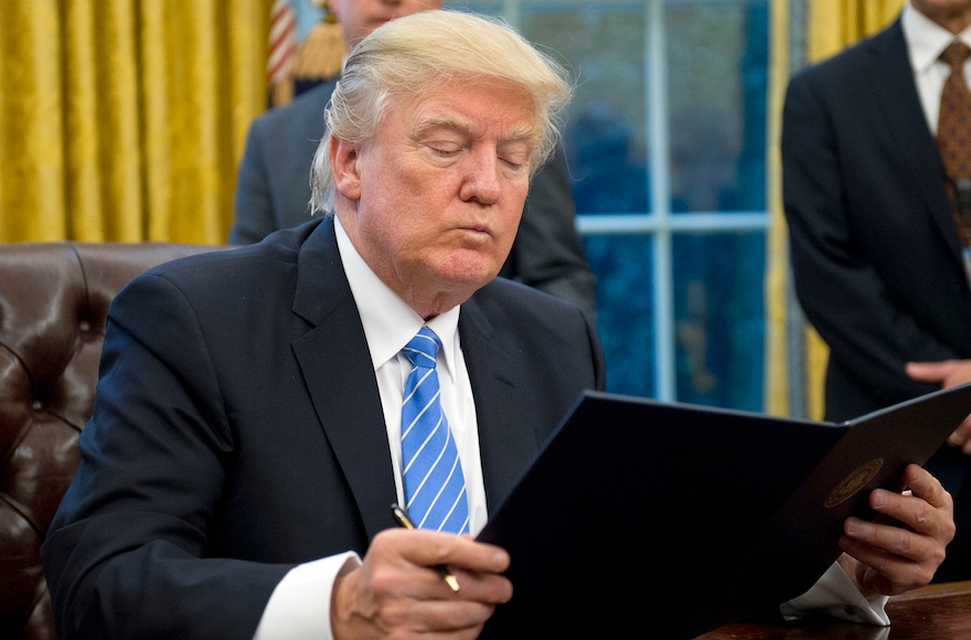 President Donald Trump reading the first of three Executive Orders he will sign in the Oval Office, Jan. 23, 2017. (Ron Sachs/Pool/Getty Images)