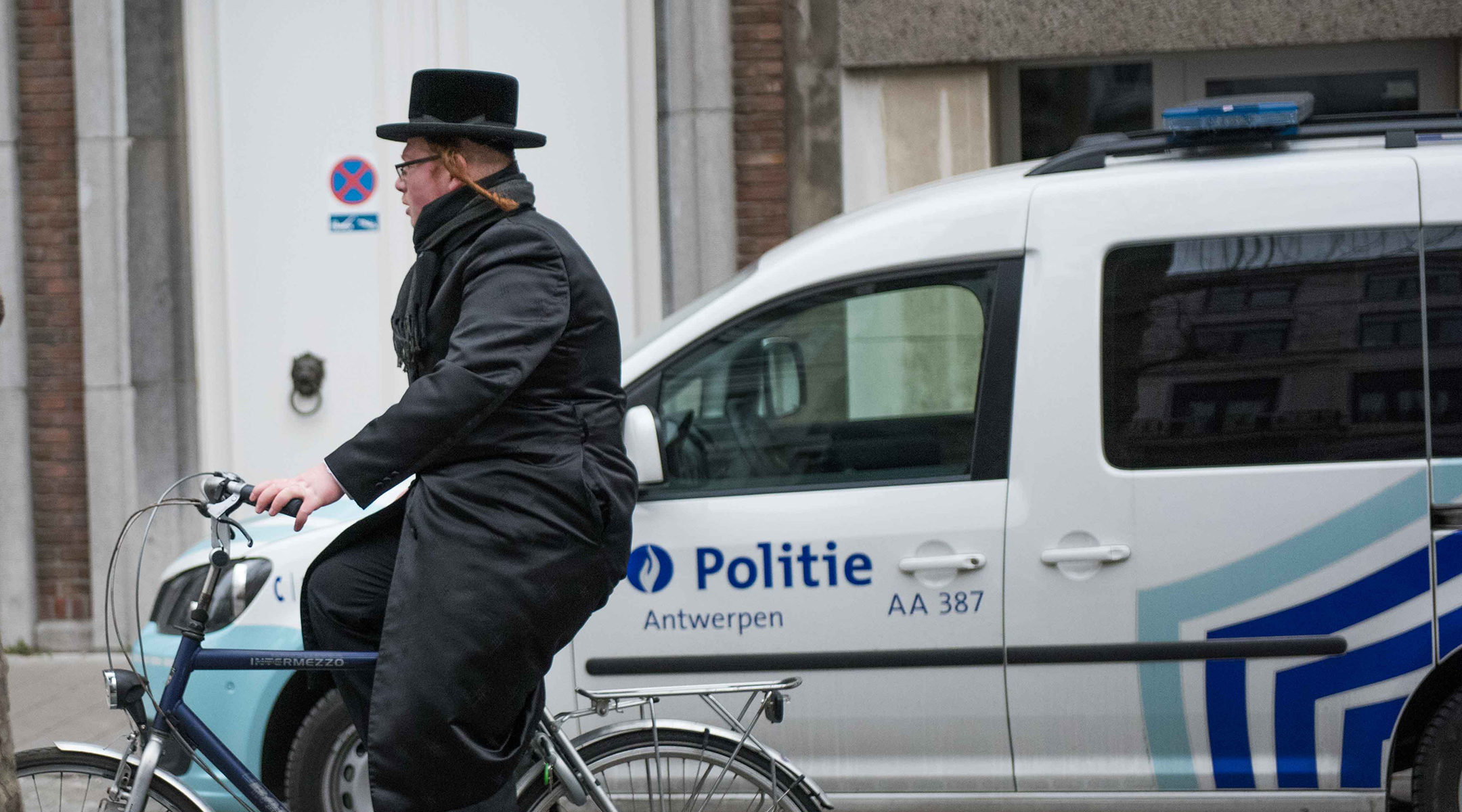 A haredi Jew cycling past a police car in Antwerp, Belgium on March 16, 2016. (Cnaan Liphshiz)