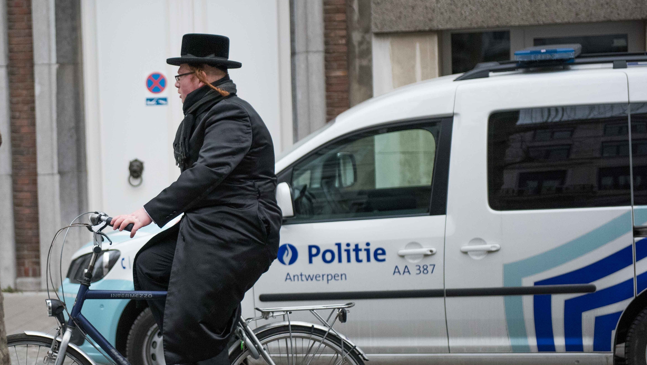 A haredi Jew cycling past a police car in Antwerp, Belgium on March 16, 2016. (Cnaan Liphshiz)