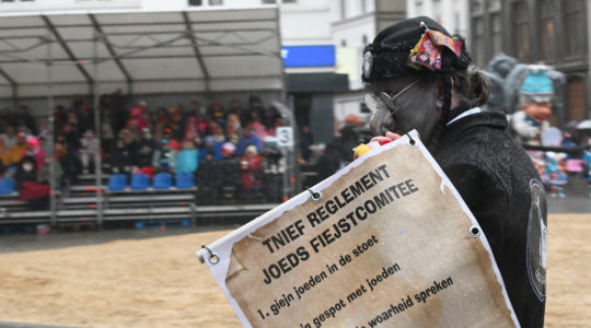 A man wearing a fake hooked nose and carrying a sign warning readers not to "tell the the truth about the Jew" at the annual procession of the carnival in Aalst, Belgium on Feb. 23, 2020. (Cnaan Liphshiz)