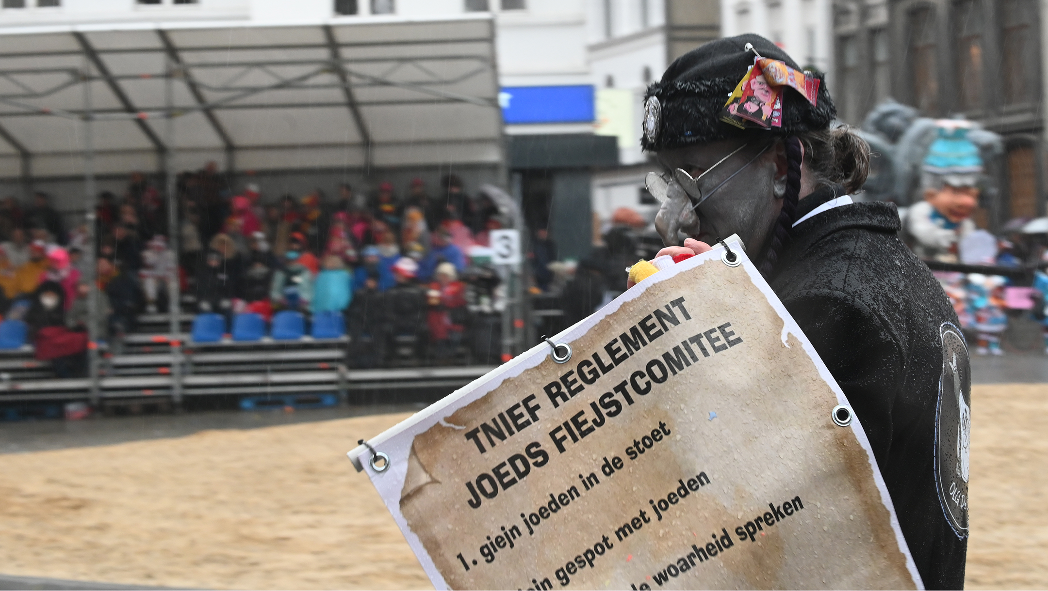  A man wearing a fake hooked nose and carrying a sign warning readers not to "tell the the truth about the Jew" at the annual procession of the carnival in Aalst, Belgium on Feb. 23, 2020. (Cnaan Liphshiz)