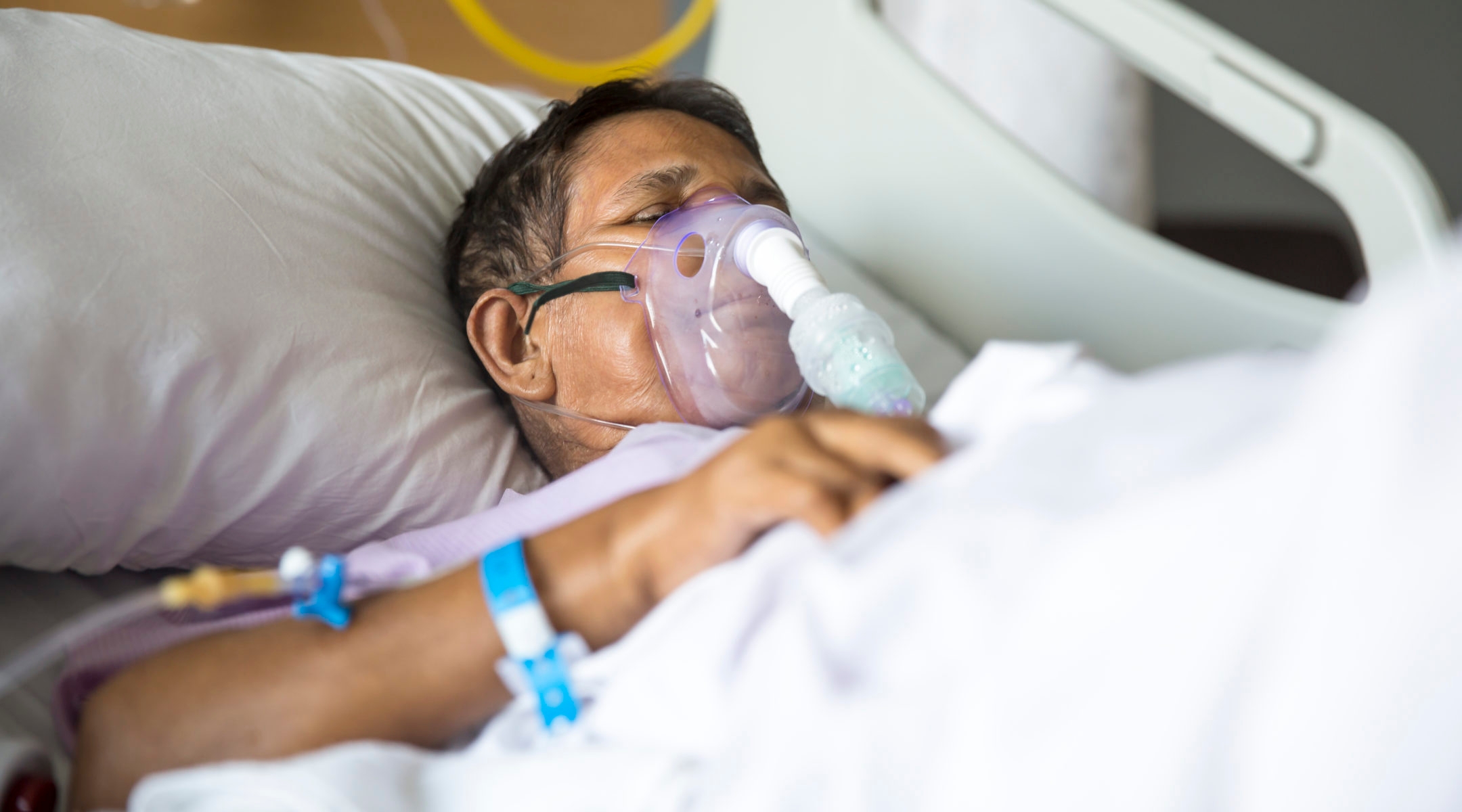 man in hospital bed with ventilator mask on