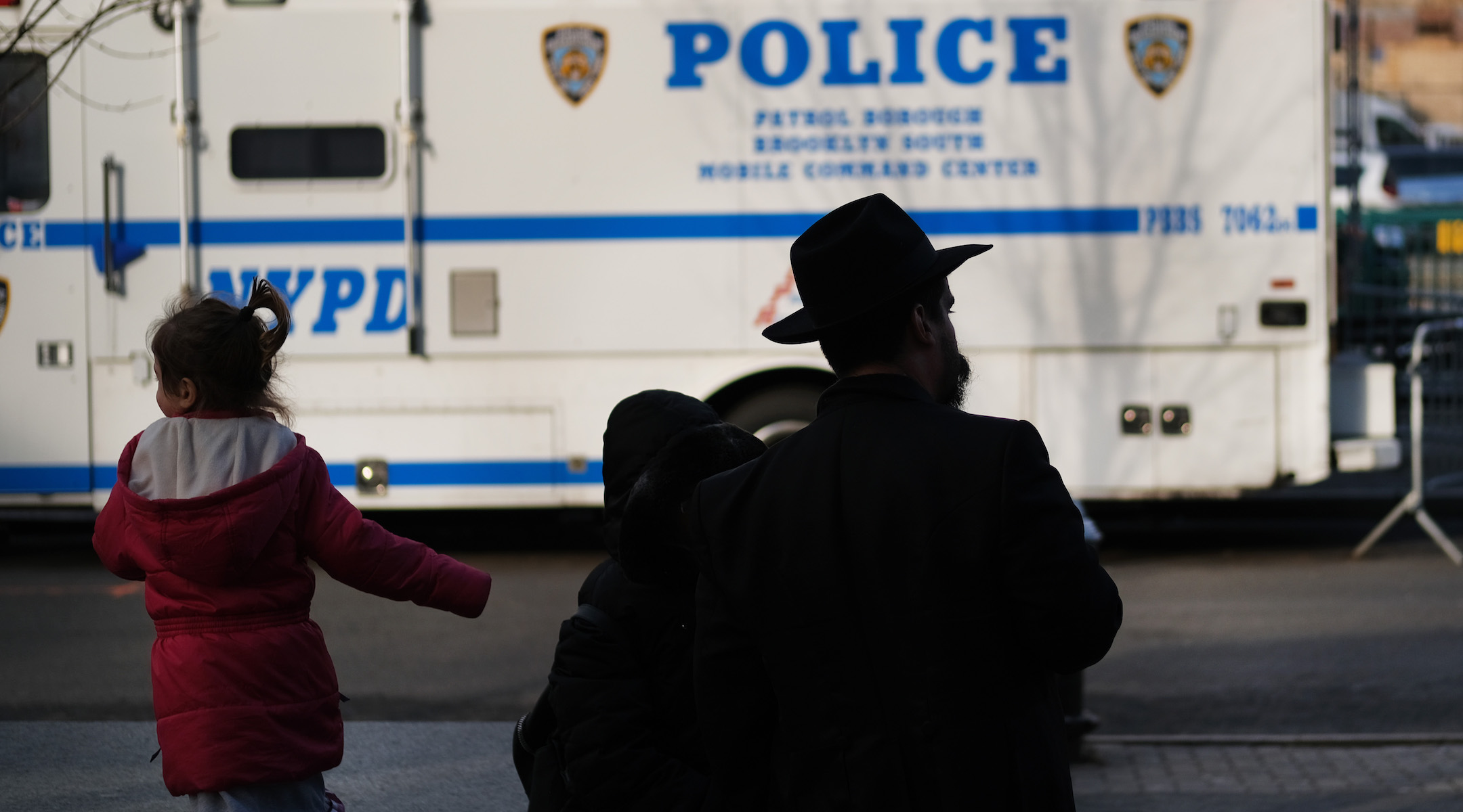 A man and girl in the Crown Heights neighborhood of Brooklyn stand opposite a police van on Dec. 31, 2019. Brooklyn was the location of more than one third of the total anti-Semitic assaults committed last year, according to the Anti-Defamation League. (Spencer Platt/Getty Images)