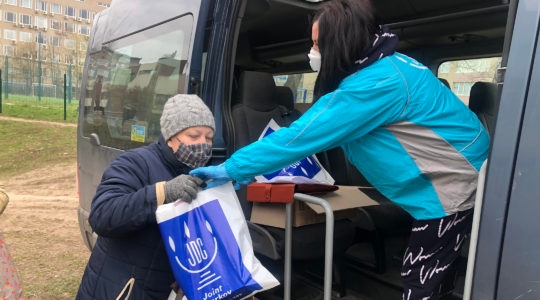 An employee of the American Jewish Joint Distribution Committee, right, hands out an aid package to a Jewish woman in Kharkiv, Ukraine during the coronavirus pandemic in March 2020. (Courtesy of JDC)
