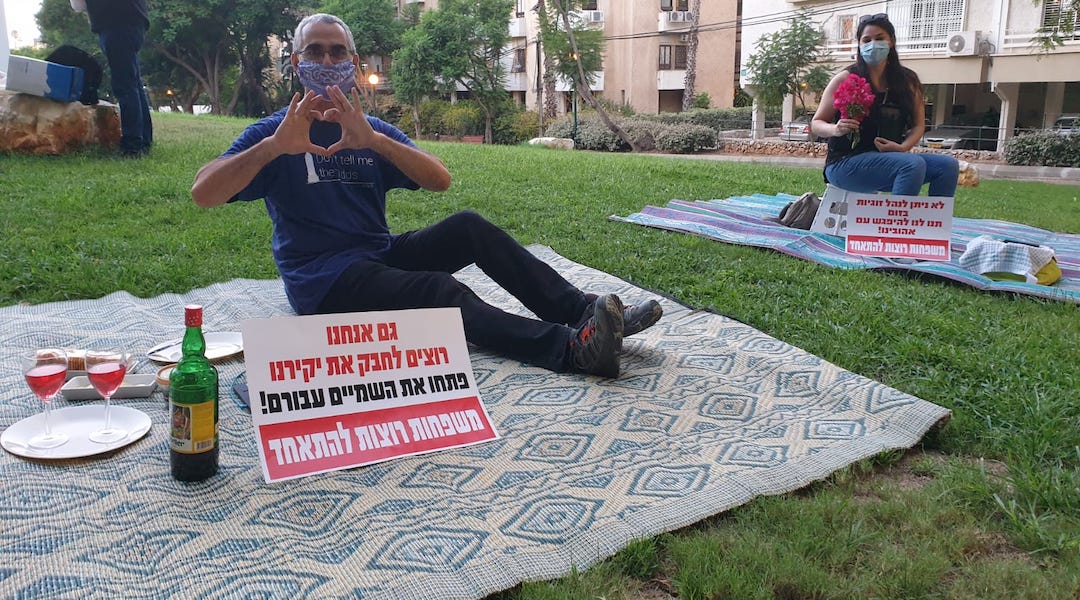 Israelis protest being separated from their significant others outside the residence of the foreign minister by having solo romantic picnics on the eve of Tu B'Av, the Jewish day celebrating love. The signs read, "We also want to embrace our loved ones. Open the skies for them. Families want to be together." (Courtesy of Plia Kettner)