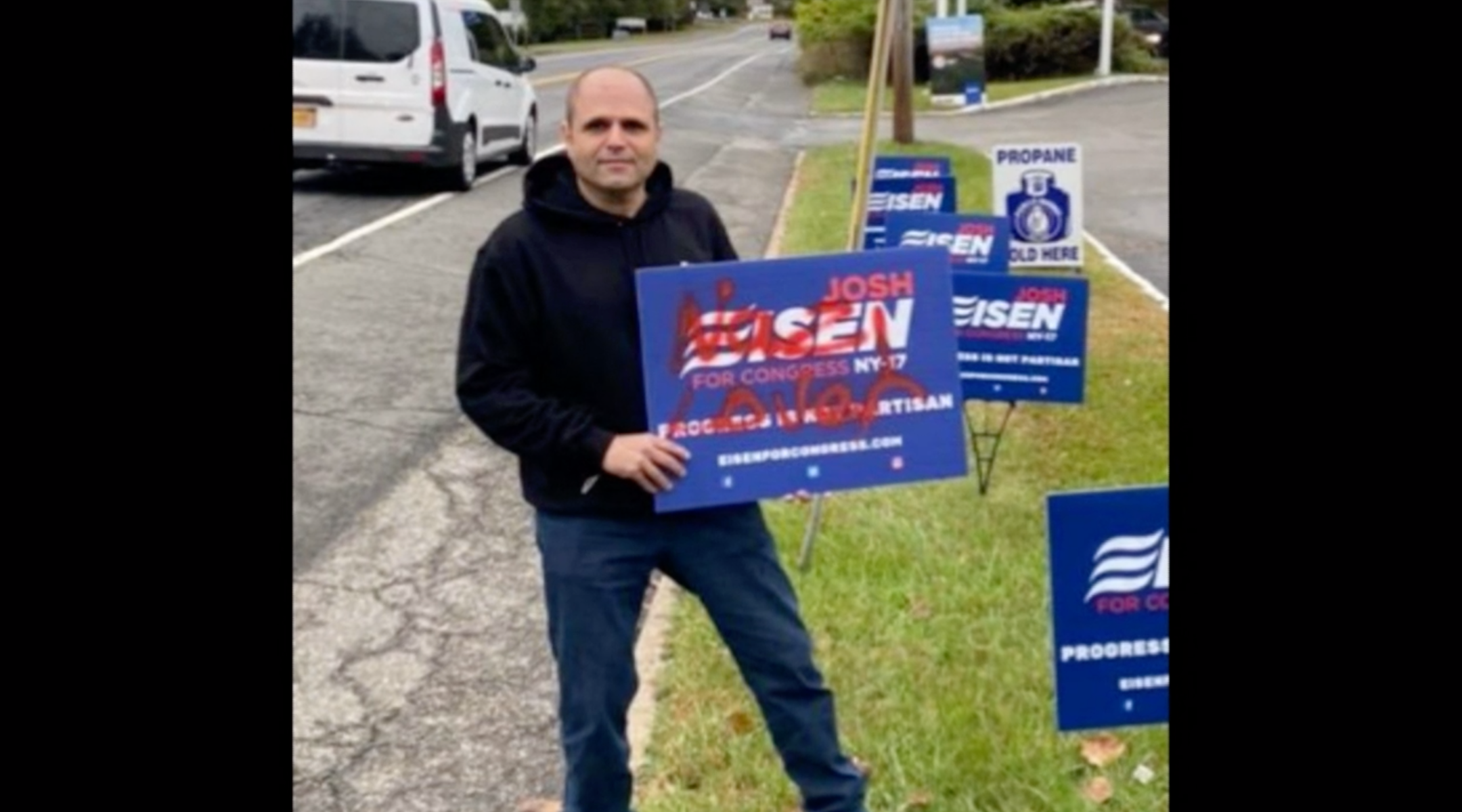 Congressional candidate Josh Eisen holds a campaign sign tagged with anti-Semitic graffiti. (Screenshot from News12)