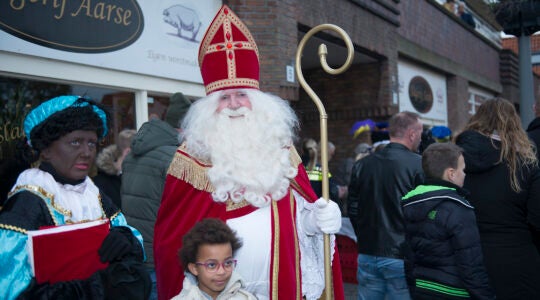 A child poses for a photo with a woman dressed as Black Pete and a man portraying Saint Nicholas in northern Amsterdam, the Netherlands on Nov. 16, 2019. (Cnaan Liphshiz)