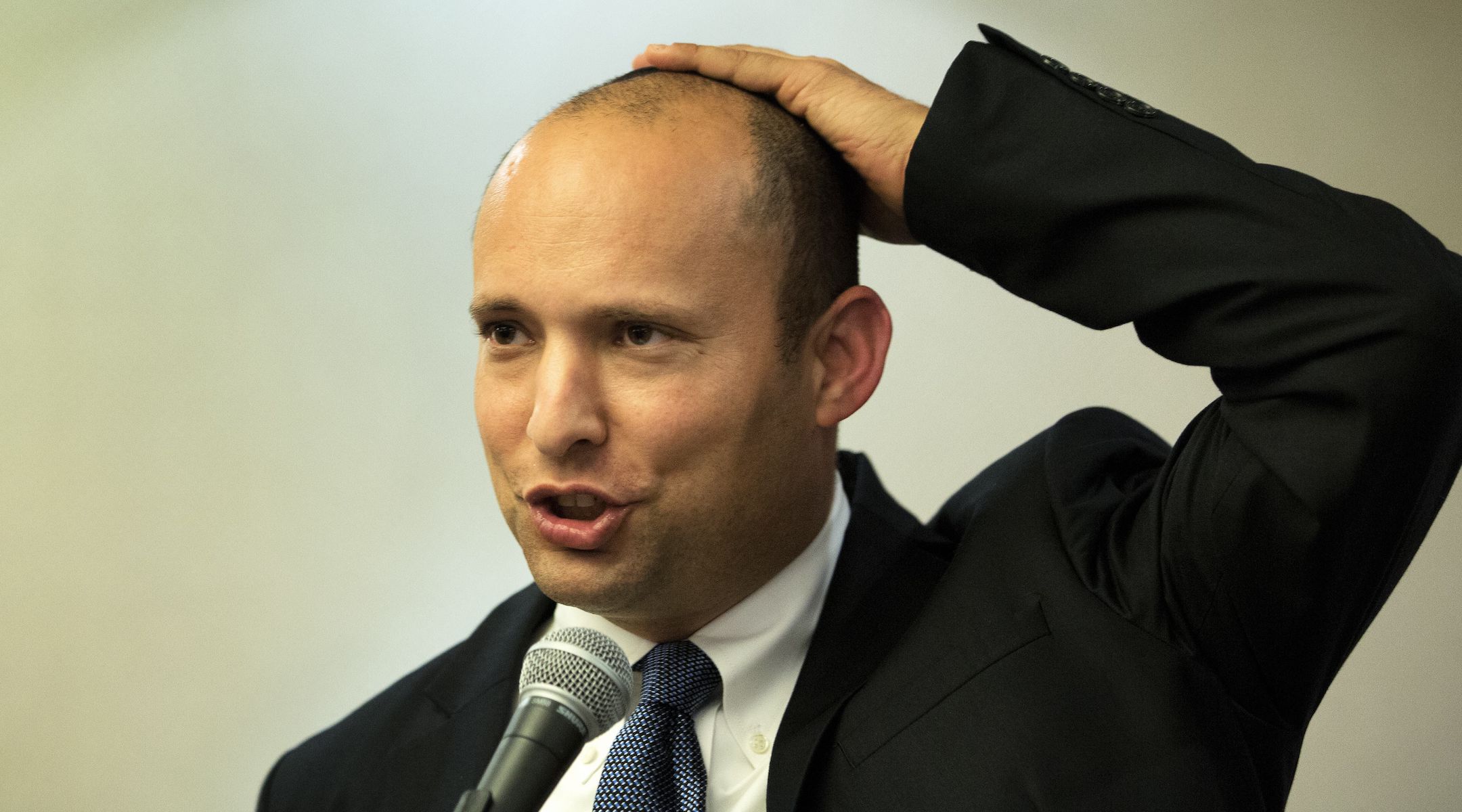 Israeli Prime Minister Naftali Bennett, pictured here in 2014 giving a speech, holds his kippah to his head. (Menahem Kahana/AFP via Getty Images)