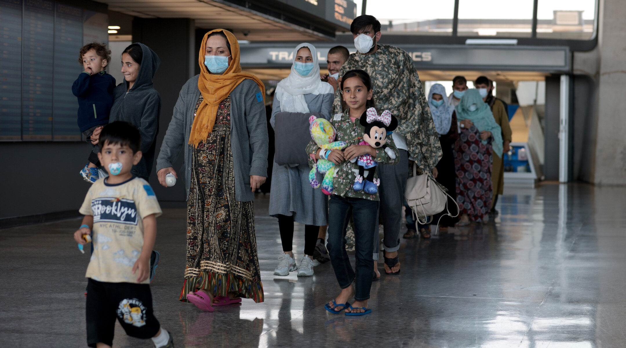 Refugees arriving at an airport; a girl clutches a Mickey Mouse doll