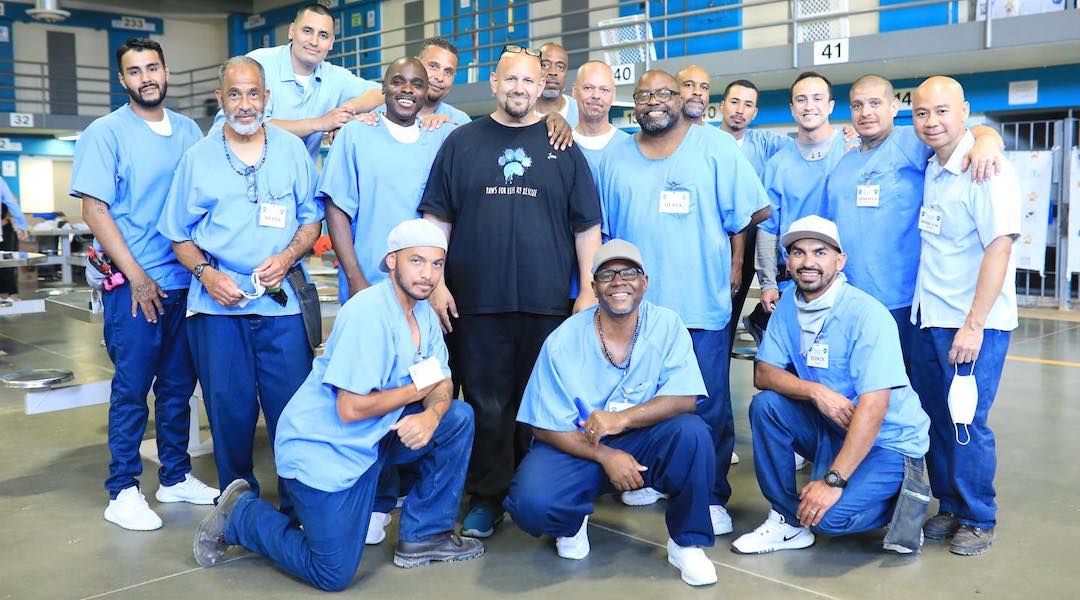 A group of incarcerated men pose for the camera around a formerly incarcerated man.