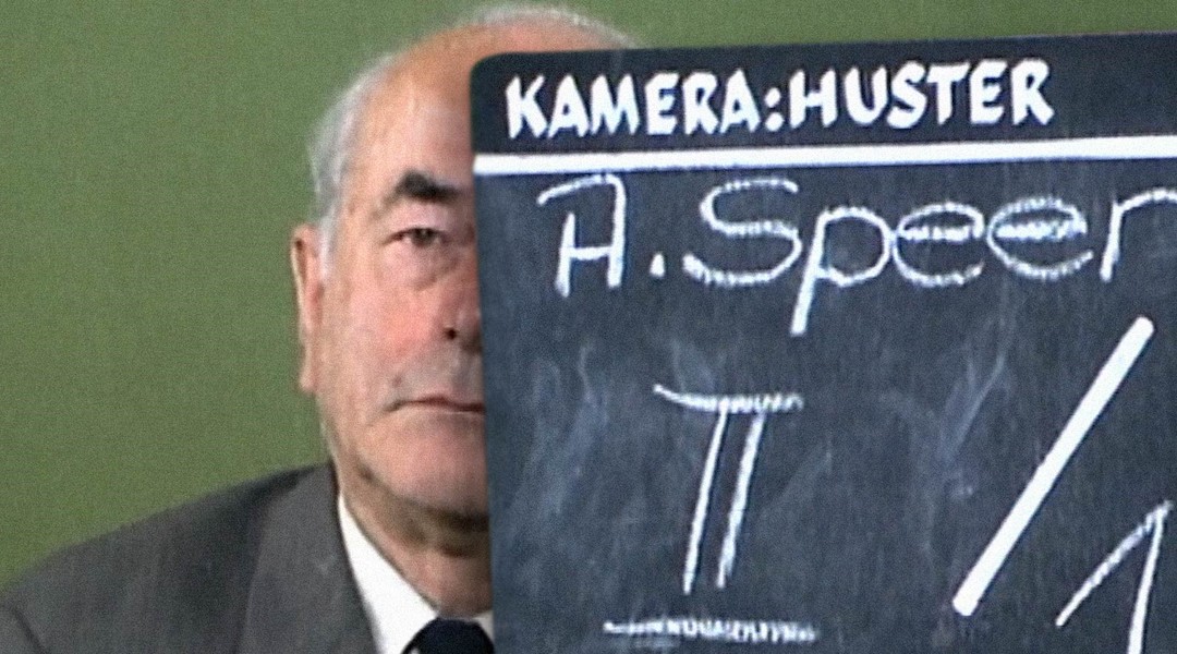 A former Nazi sits behind a film clapboard
