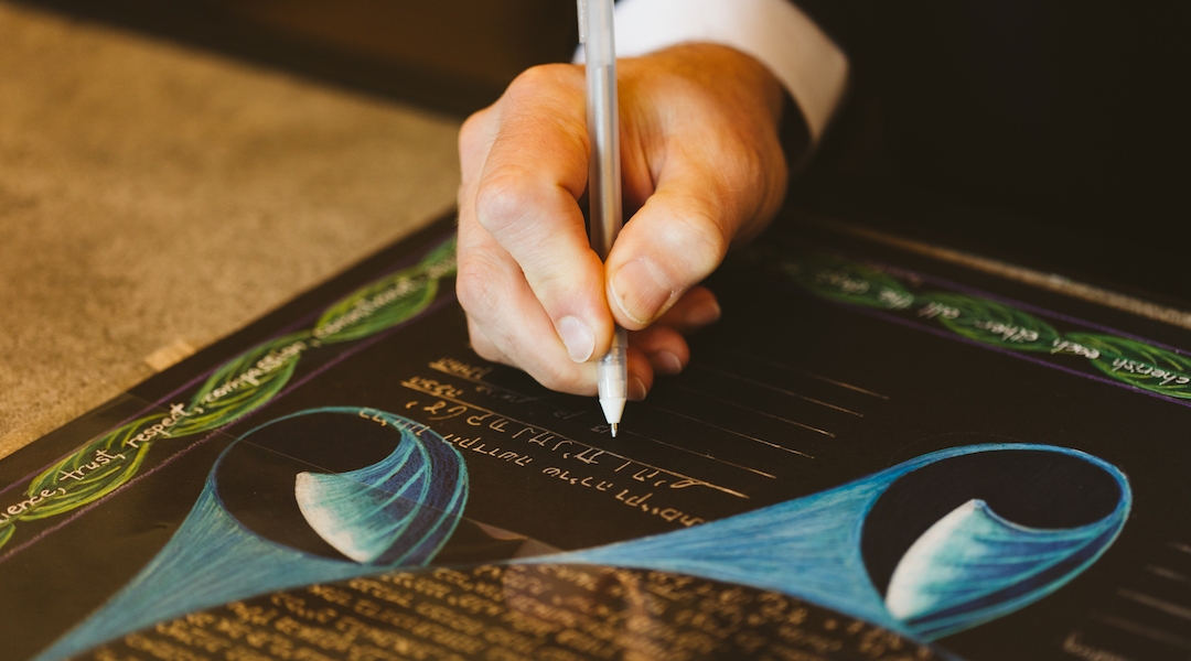 A man's hand signing a colorful ketubah