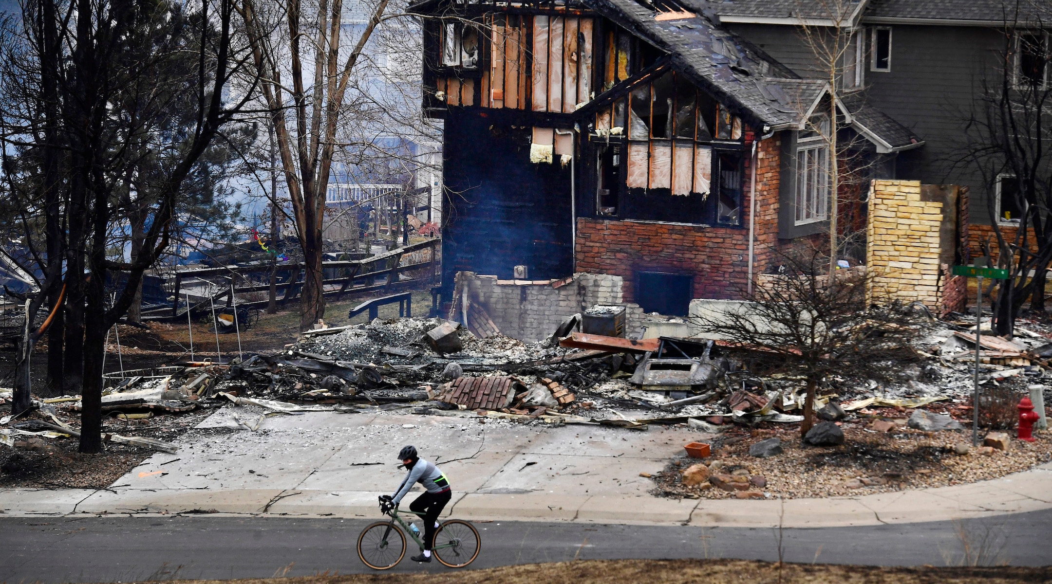 A man on a bike rides by a burned home