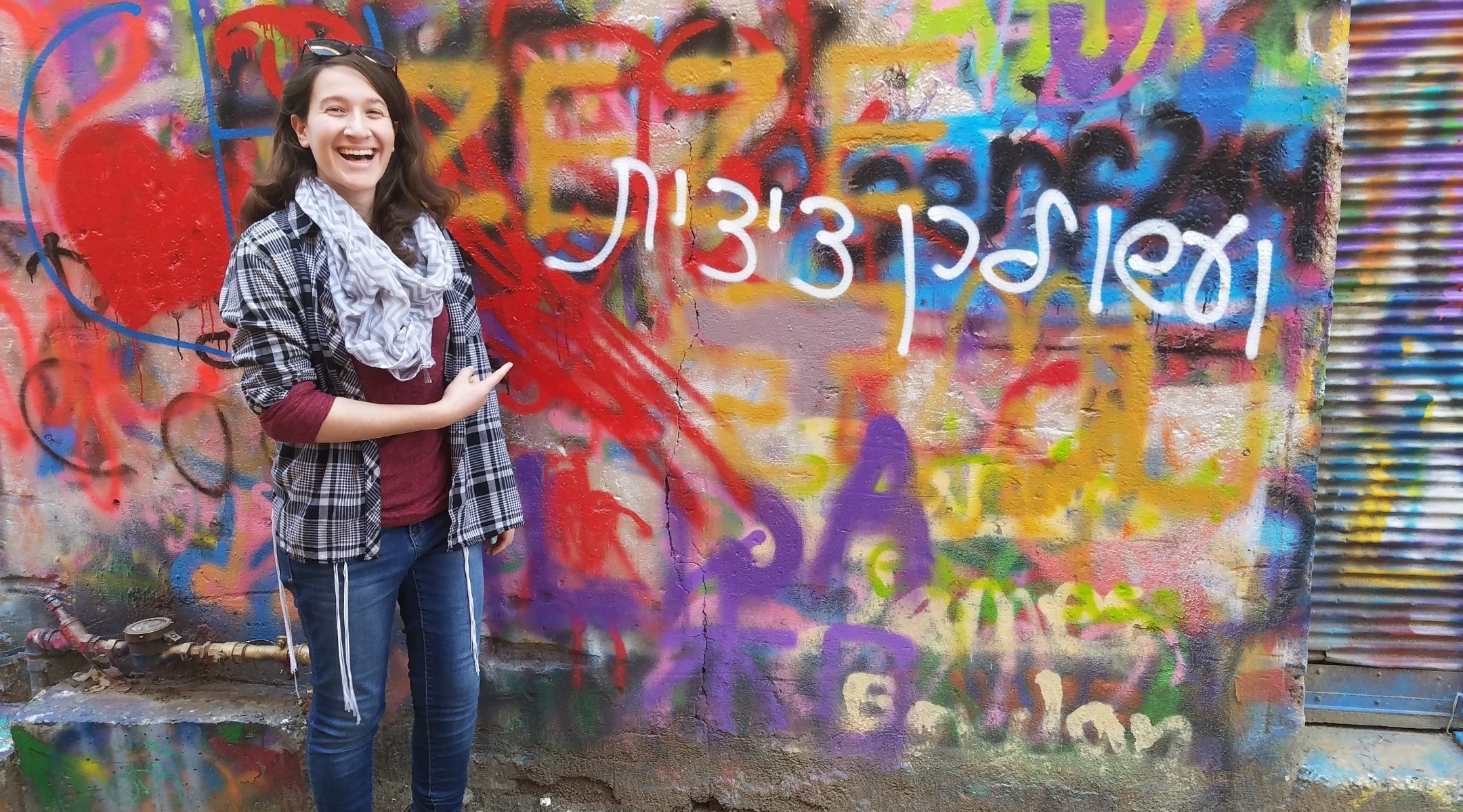 Rachel Schwartz stands in front of a piece of graffiti that plays on the commandment to wear tzitzit, written in the Hebrew feminine. (Courtesy of Rachel Schwartz)