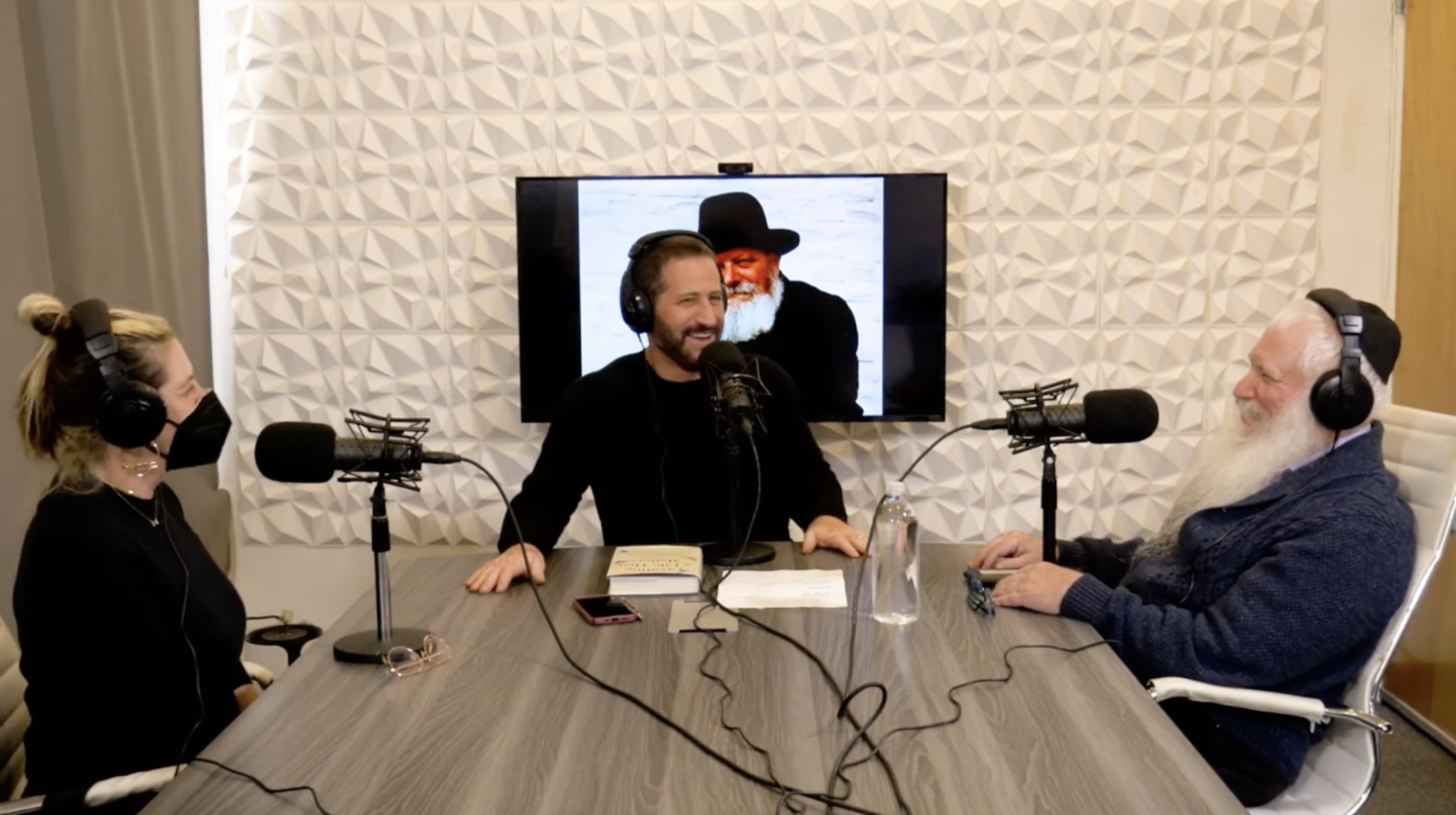 Comedian Modi Rosenfeld Rosenfeld speaks with Rabbi Manis Friedman, right, and comedian Periel Aschendbrand on his podcast in November 2021. A portrait of Rabbi Menachem Mendel Schneerson, the last rebbe of the Chabad Orthodox movement, is behind Rosenfeld. (Screenshot via YouTube)