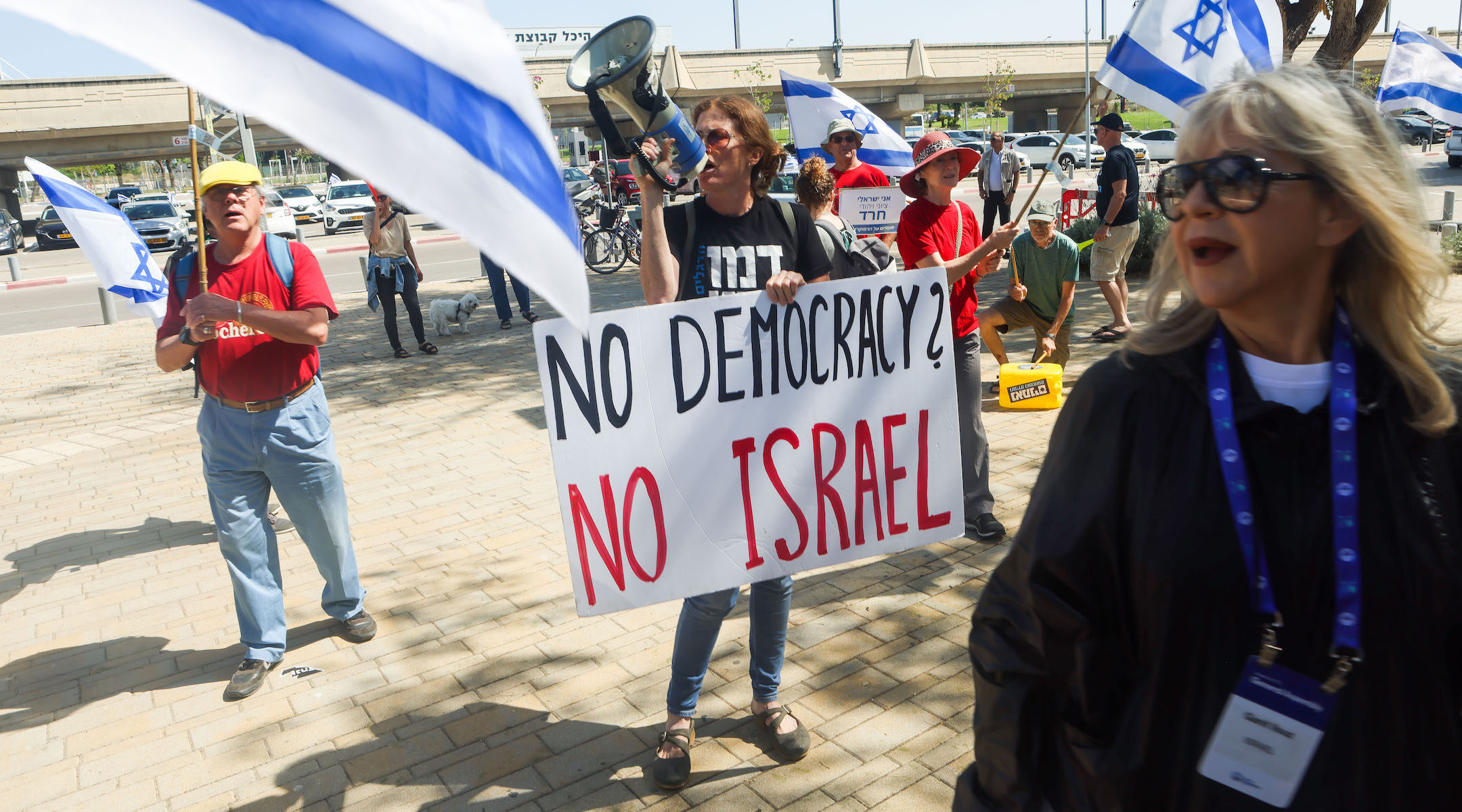 A protester demonstrates at the 2023 Jewish Federations of North America General Assembly in Tel Aviv as a conference attendee walks past. (Courtesy of JFNA/Amnon Gutman)