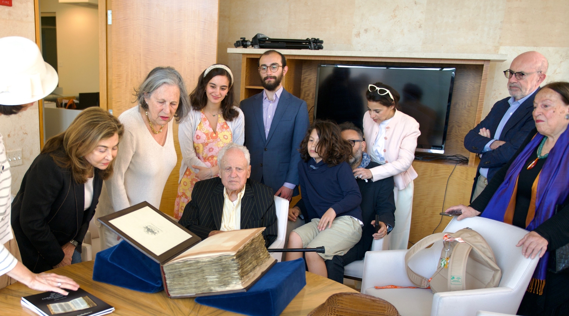 Alfred Moses (center, seated) examines the Codex Sassoon surrounded by family and friends. (Perry Bindelglass for The American Friends of ANU The Museum of the Jewish People)