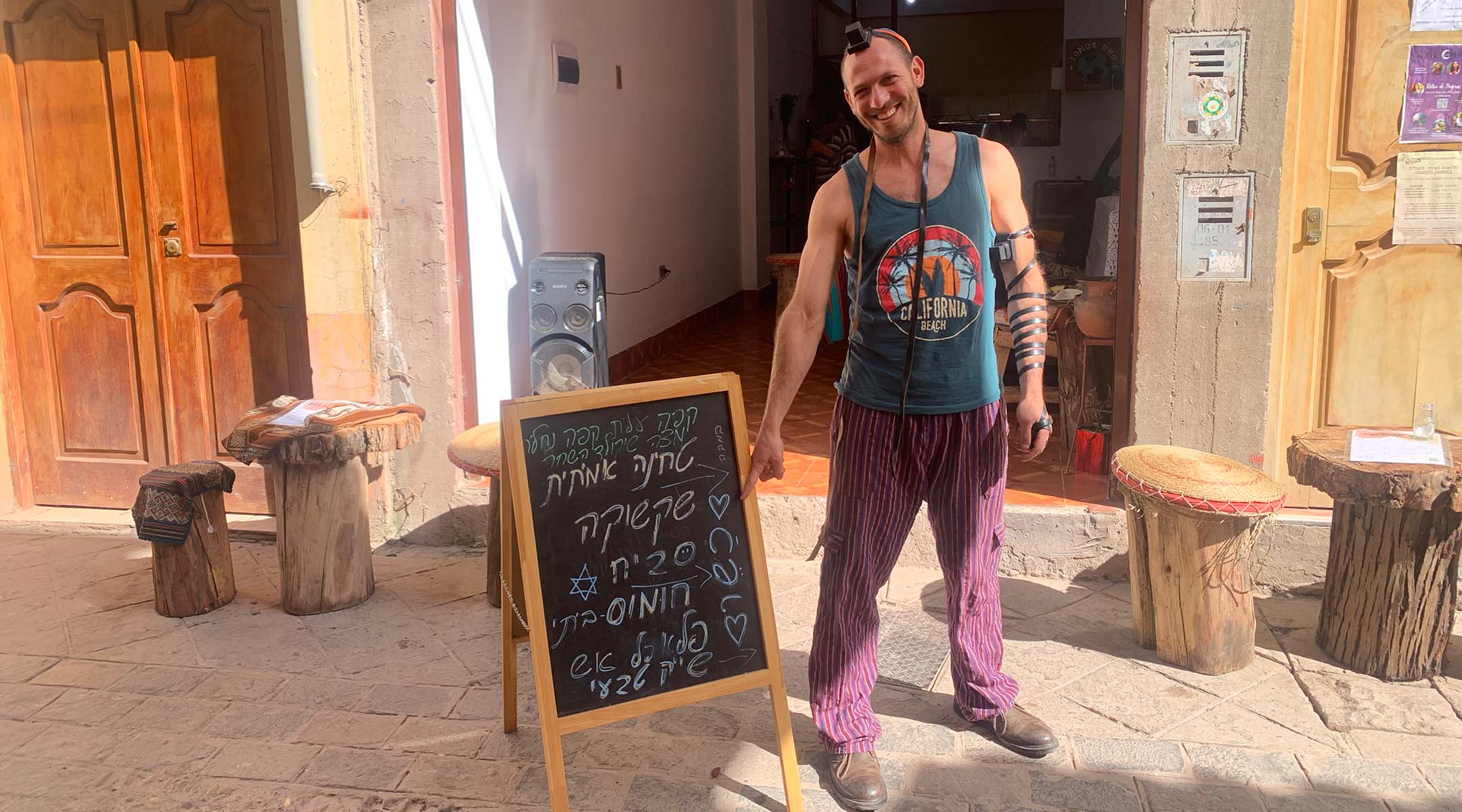 Aminadav Shvat stands outside his restaurant in Pisac, next to an easel advertising some of the Israeli dishes he serves. (Jacob Kessler)