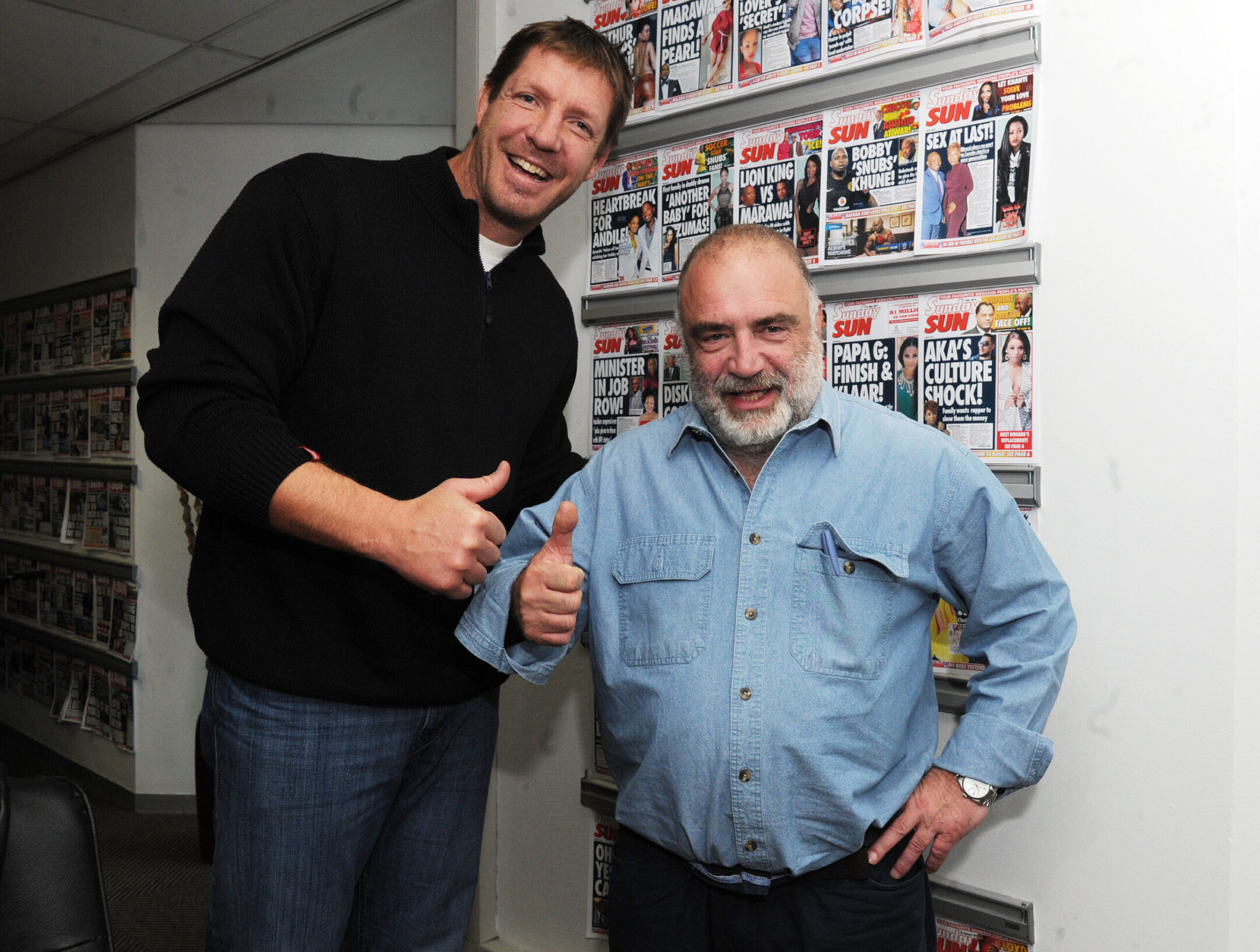 Jeremy Gordin, at right, stands in front of covers of the Sun, the South African tabloid he oversaw for many years. (Courtesy Gordin family)