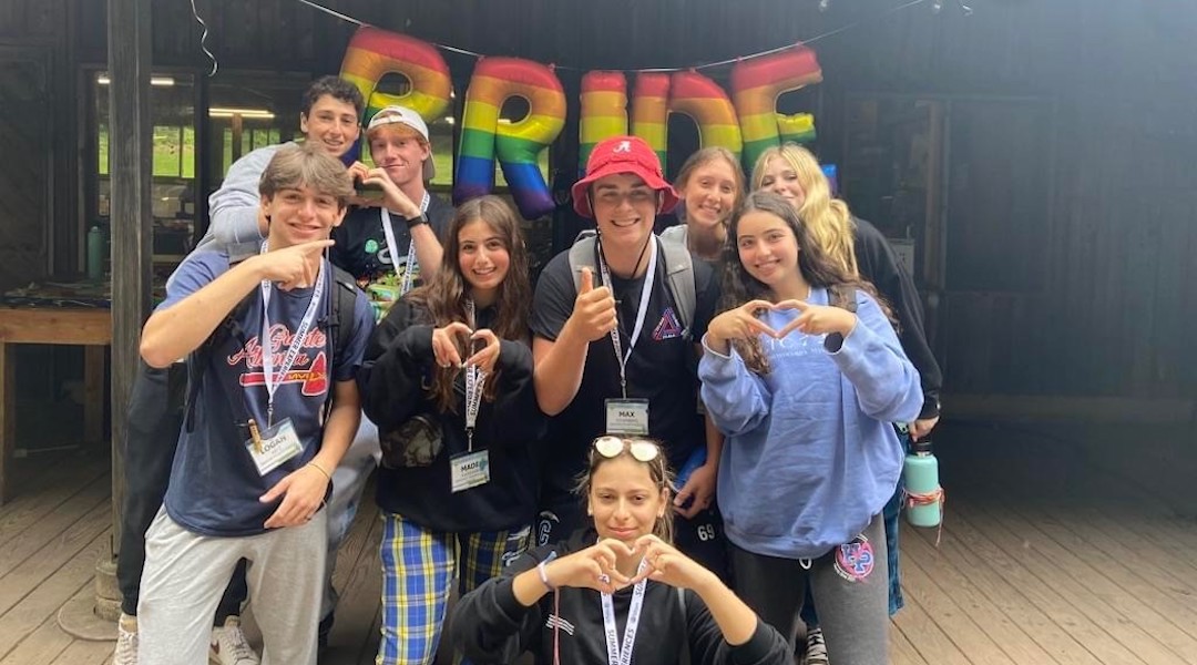 Teenagers making a heart sign with a "PRIDE" banner behind them