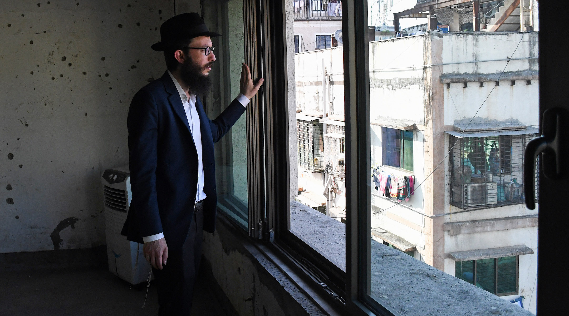 Rabbi Israel Kozlovsky, director of Mumbai's Chabad center, looks out of a window of the center, in front of a wall pock-marked with bullet holes from the 2008 terror attack. (Ashish Vaishnav/SOPA Images/LightRocket via Getty Images)