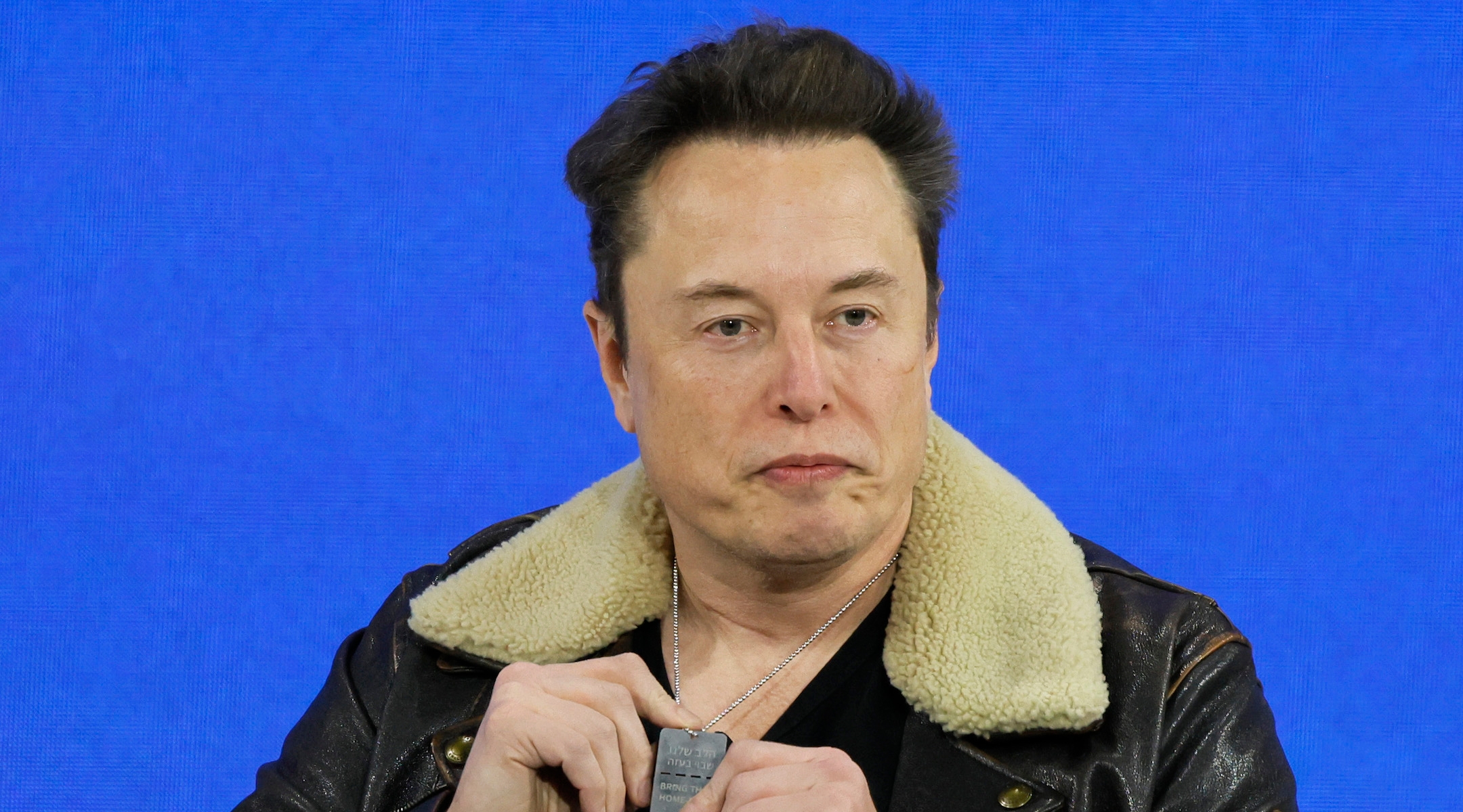 Elon Musk holding up a dog tag supporting the release of Israeli hostages onstage at a conference
