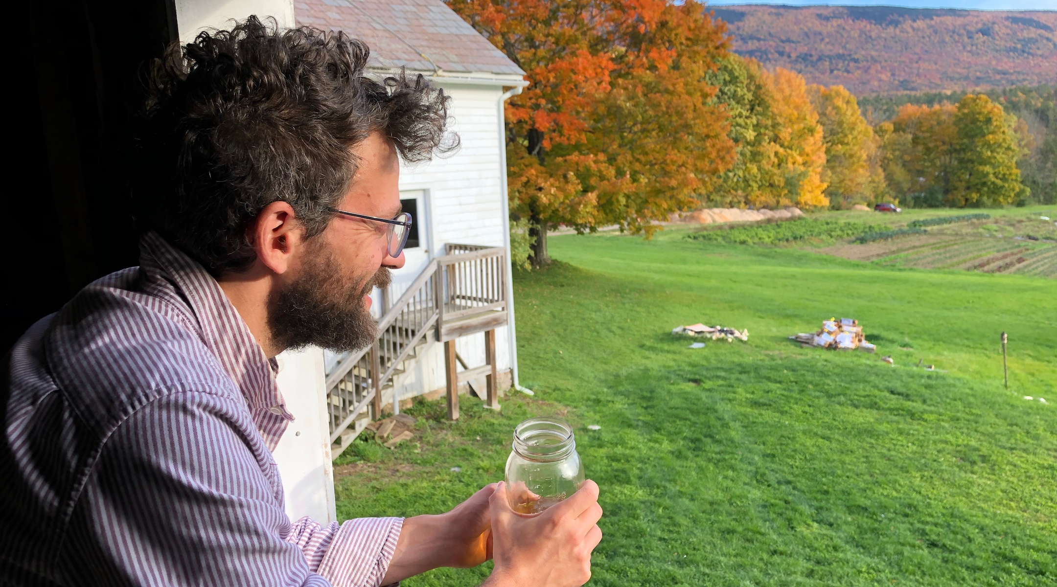 A young man overlooks a farm holding a drink in a mason jar