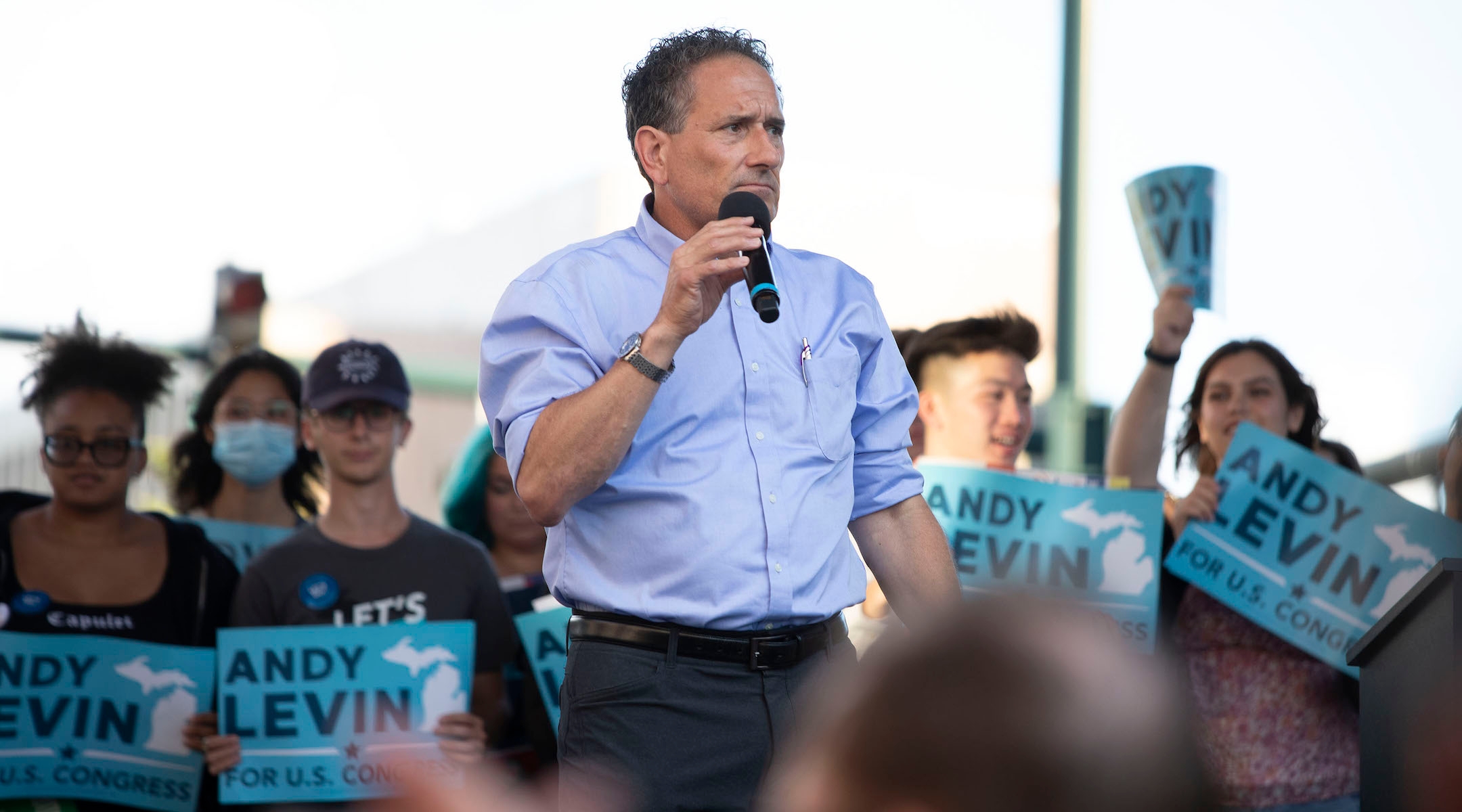 A politician standing on a rally stage with his sleeves rolled up