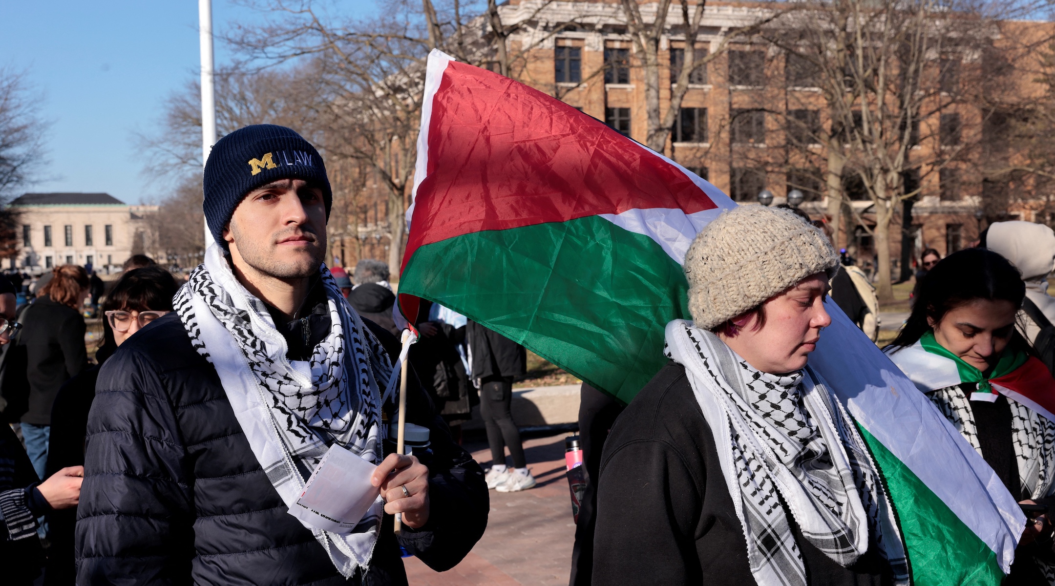 Protesters wearing keffiyehs and carrying Palestinian flags march on a college campus