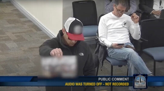 A man wearing dark sunglasses and a blurred-out hat holds up a blurred-out white supremacist handout during a city councio public comment period