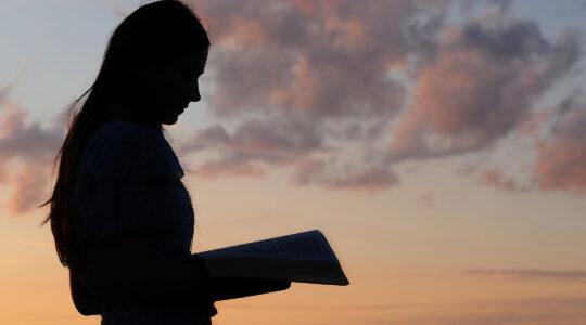 Silhouette of a young girl reading from bible in sunset light.