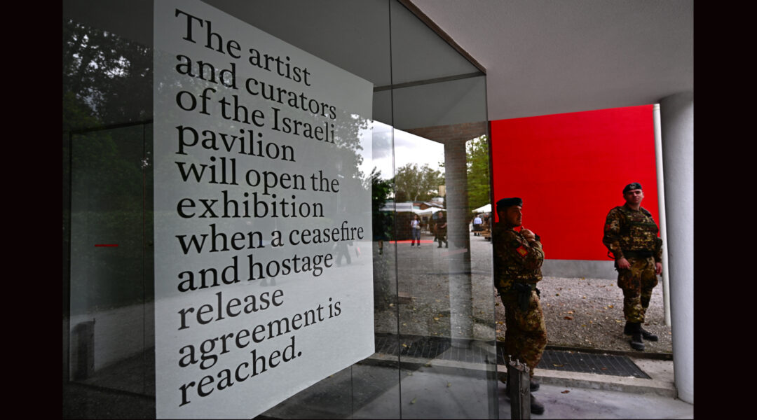 The exterior of the Israeli pavilion at the Venice Biennale, covered with a pro-ceasefire protest message, with a soldier standing guard