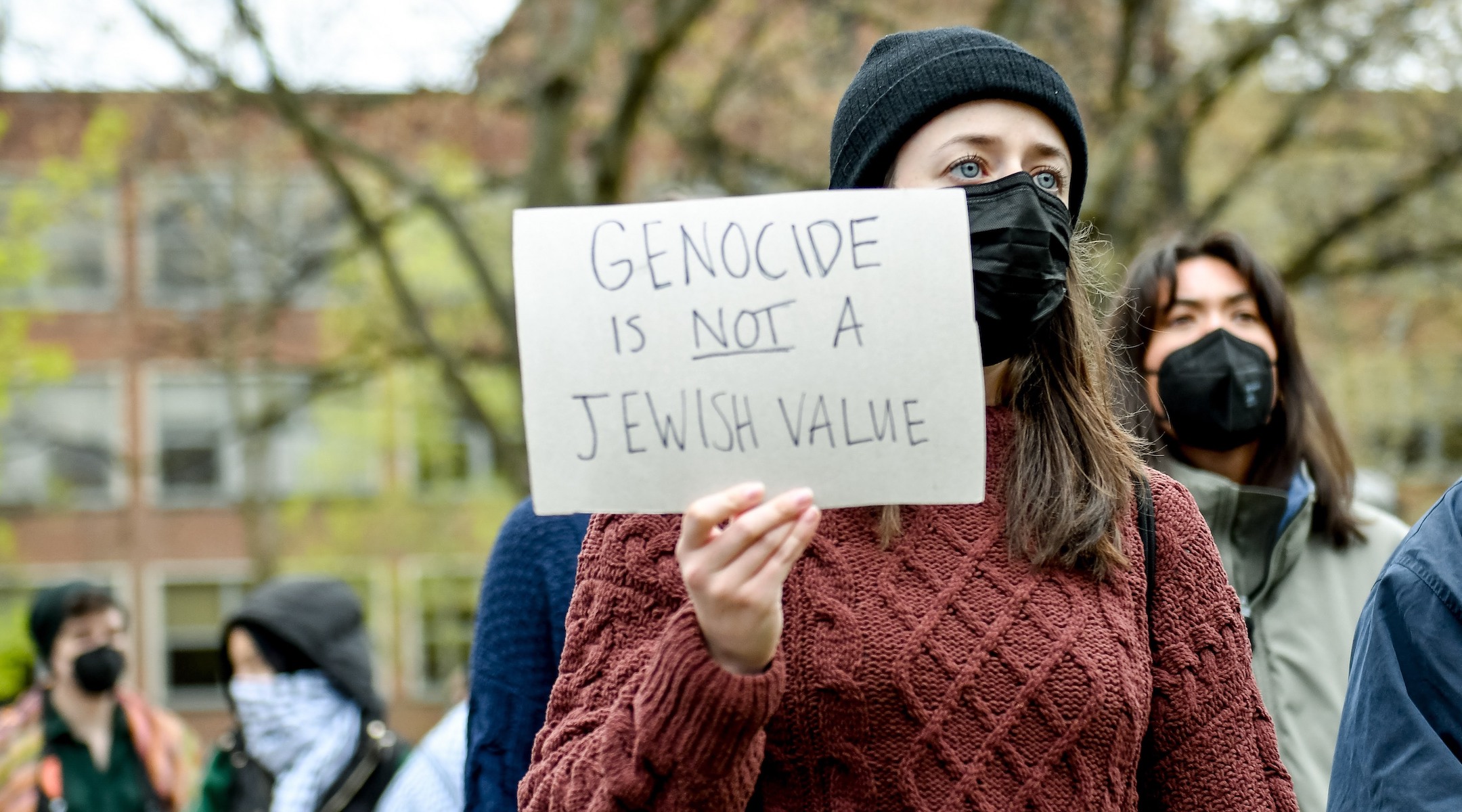A young woman holds up a sign reading "Genocide is not a Jewish value"