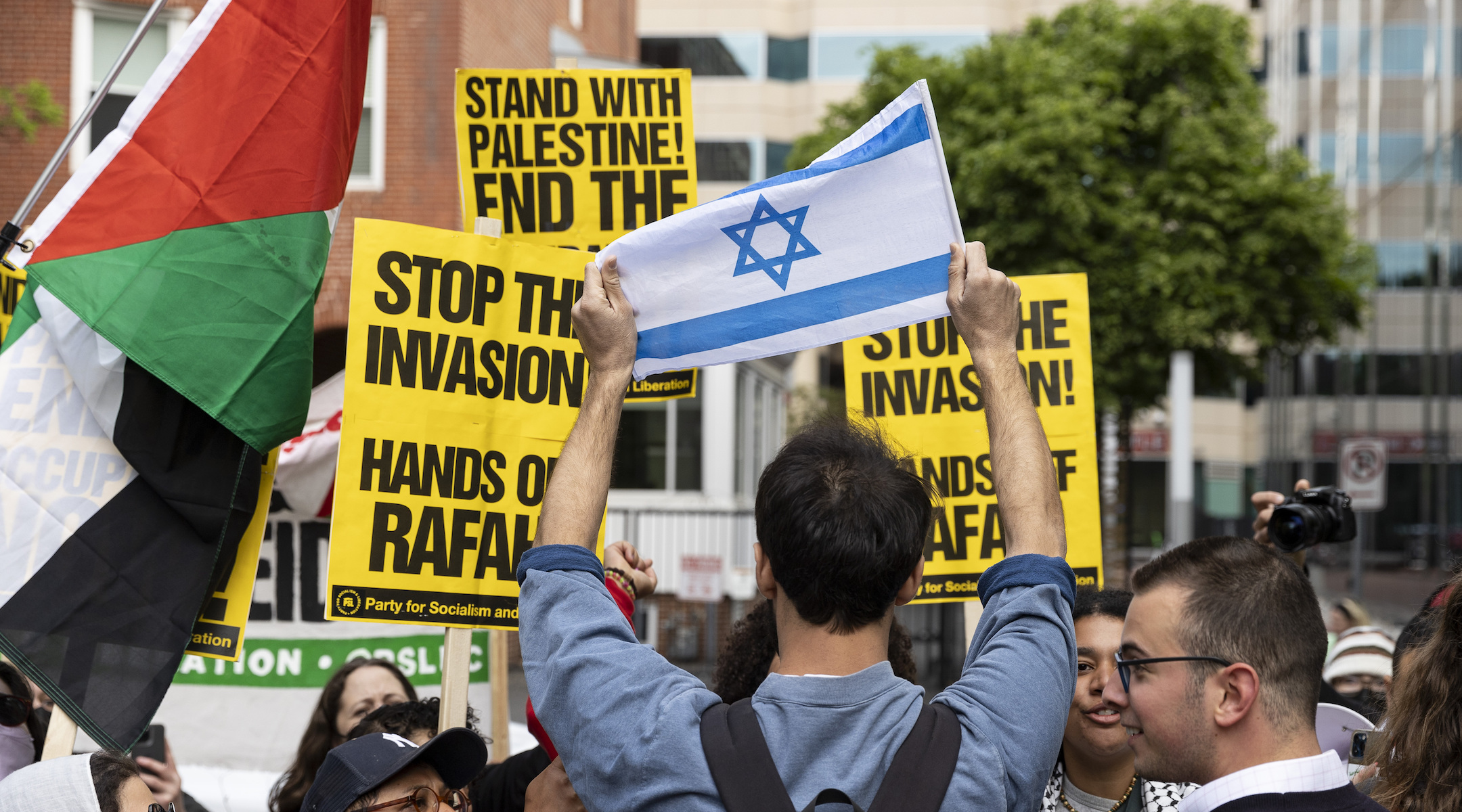 A man holding a pro-Israel flag facing a crowd holding pro-Palestinian flags