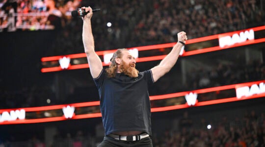 A wrestler gestures in the air holding a microphone