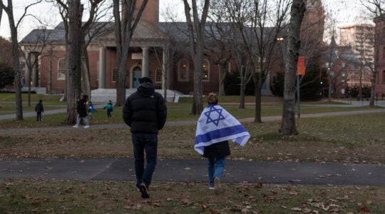Two people, one draped in an Israeli flag, walk across Harvard's campus