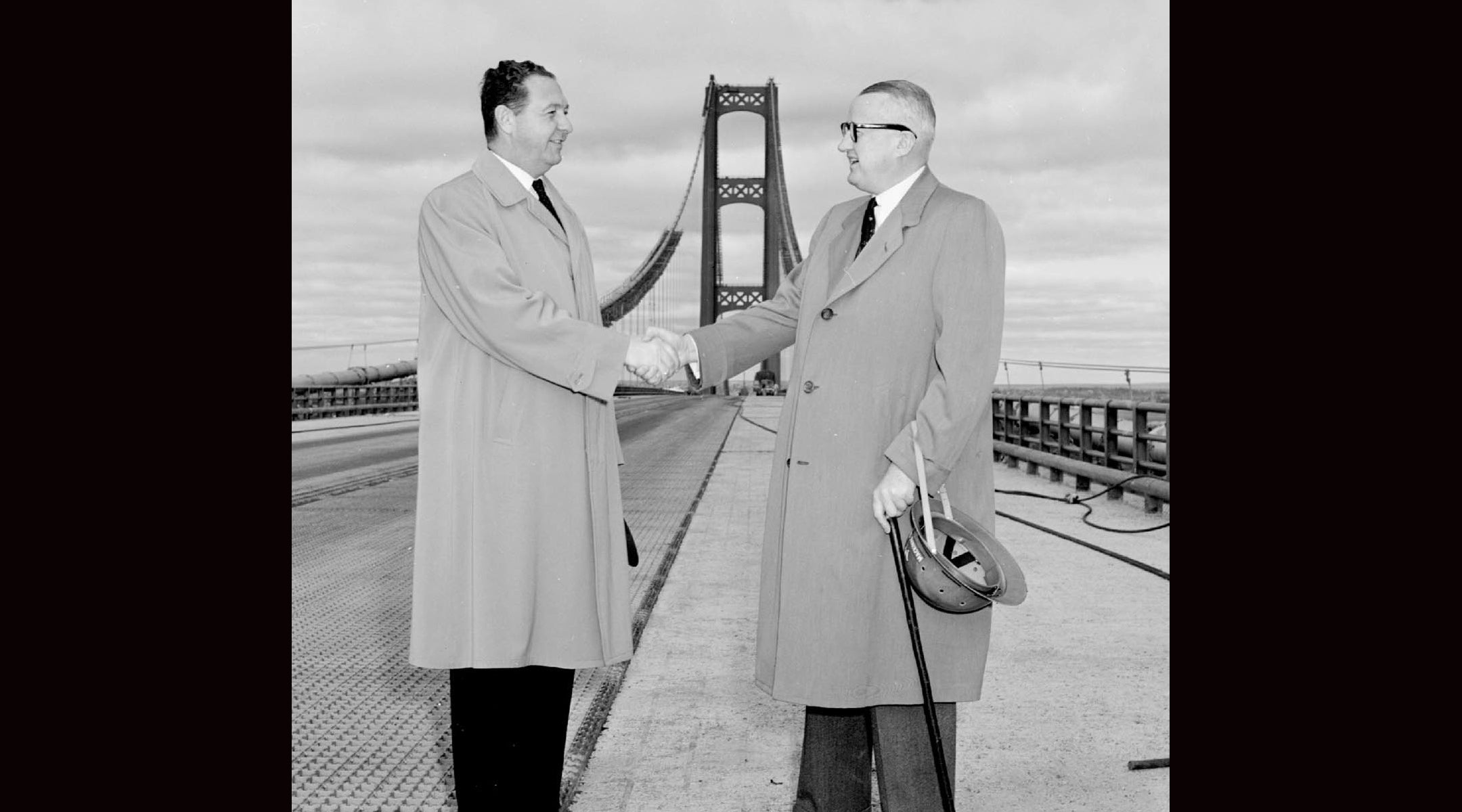Two men shake hands on a bridge