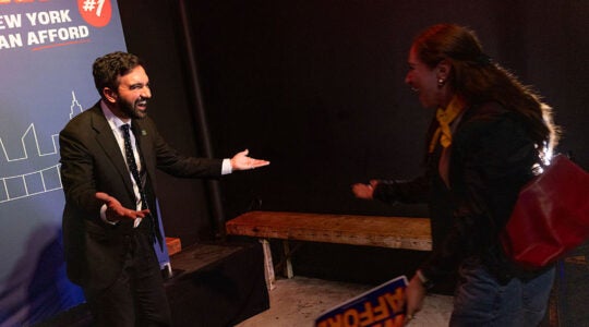 Zohran Mamdani with arms extended speaking with a supporter