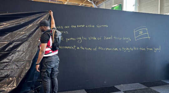 A security personnel works to hide a graffiti reading "Behind these walls are the best defense systems used by many countries. These systems are protecting the state of Israel these days. The French government, in the name of discrimination is trying to hide them from you!", on a panel of the Israel Aerospace Industries (IAI) Israeli Pavillon during the International Paris Air Show at the Le Bourget Airport on June 16, 2025.